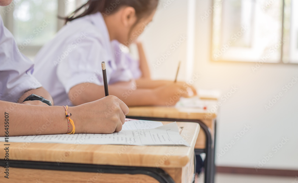 Students using pen writing information on white answer paper in high school, Asian exams room, Tests or examination is assessment intended to measure knowledge, skill, aptitude, Education Concept Students using pen writing information on white answer paper in high school, Asian exams room, Tests or examination is assessment intended to measure knowledge, skill, aptitude, Education Concept