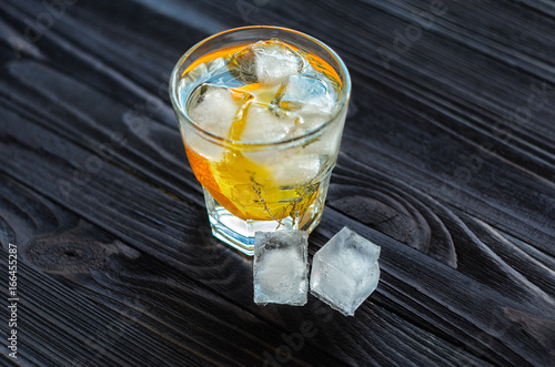 Cocktail with citrus fruits, sprig of rosemary and cubes of ice on dark wooden table photo