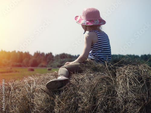 A small child sits on a haystack.