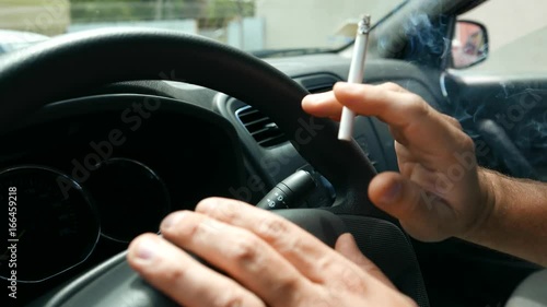 Smoking tobacco cigarettes while driving, nicotine addiction. Hand tremor. Male driver is nervous and smokes in the car. Traffic congestion