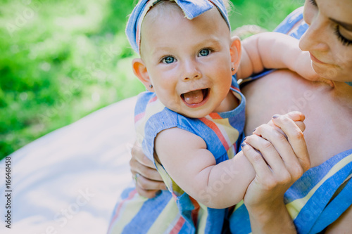 Woman in blue striped dress raises up her little daughter in the same clothes in the park. happy family