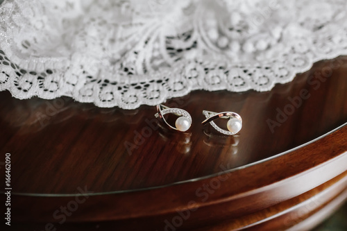 Bridal pearl earrings on brown wooden table with white wedding veil