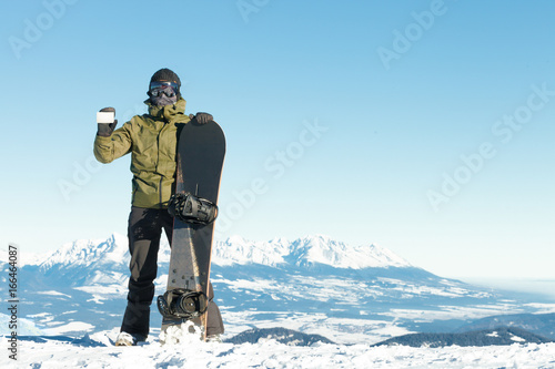 Snowboarder holding blank lift pass in one hand and snowboard in another with beautiful mountains on background