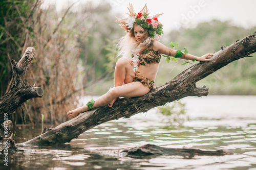 Konstfotografi Beautiful little girl in image of nymph sits on tree slanted above water