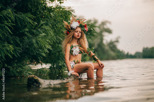 Obraz na plátně Beautiful little girl in image of nymph sits on tree trunk in water