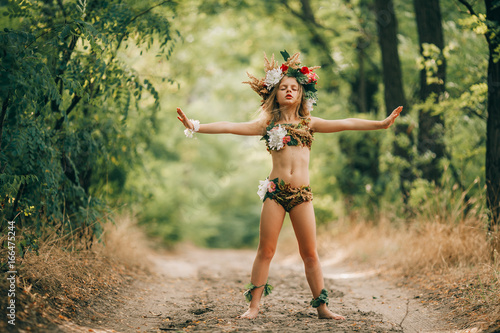Beautiful little girl in image of nymph dryad stands in forest road and does spell. photo