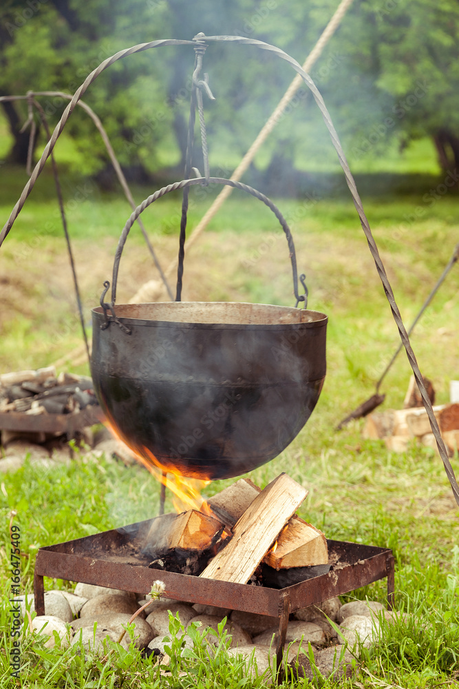 Black old metal pot hanged over fire, camping kitchen, vertical Black old metal pot hanged over fire, camping kitchen, vertical