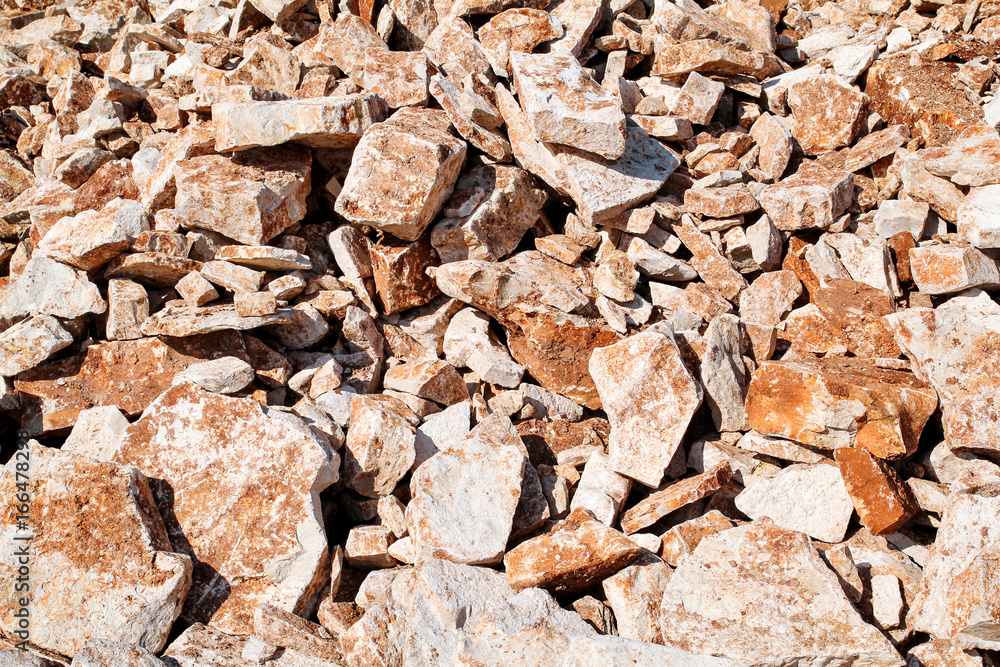Fototapeta premium Part of a stone pile of rocks for construction and boulders piled, close up. Brown Granite. A large pile of limestone in quarry. Pile of gravel and construction material.