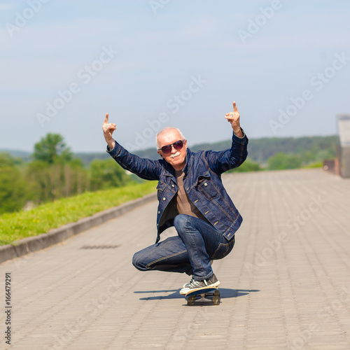energetic senior man enjoying riding a skateboard. The concept of life satisfaction. Portrait of a positive gray-haired man with a skateboard. winner concept.