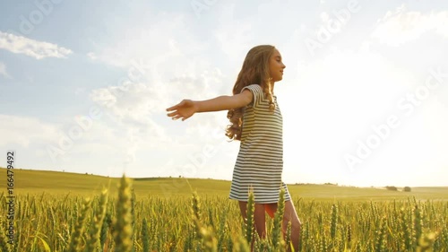 Little girl with curly hair spinnig in the golden wheat field at blue sky background. photo