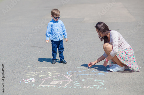 Mom and little son are painting with crayons on the road.