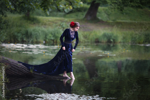 Beautiful girl in a long blue dress on the shore of a forest lake.