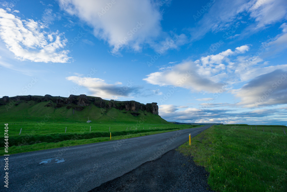 Iceland - Blue sky over street between green meadow and volcanic rocks at dawn