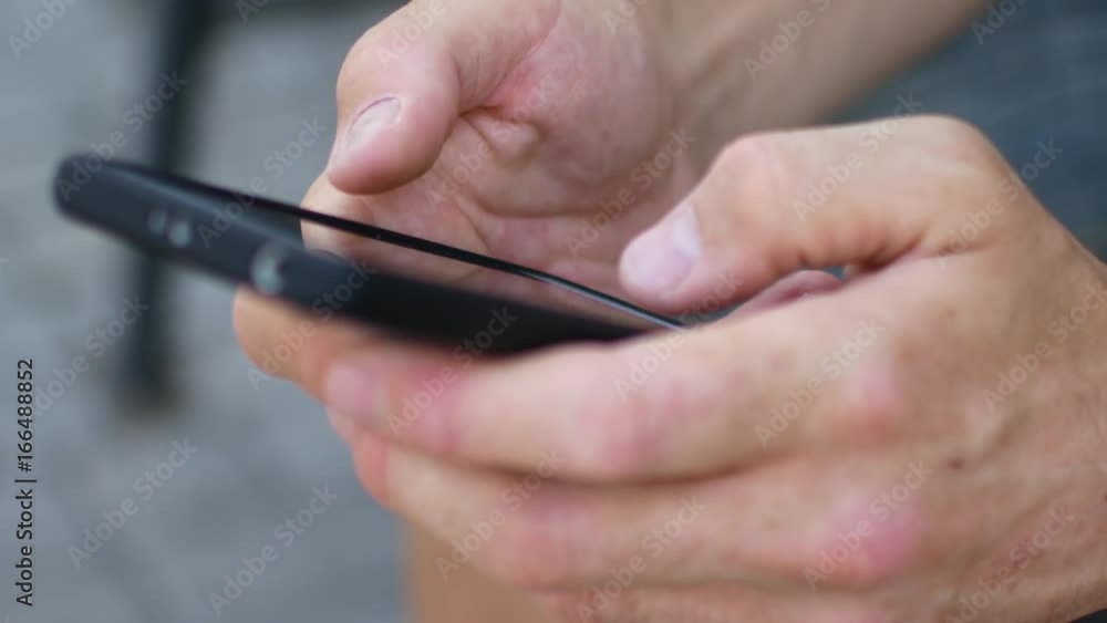 A close-up of the hands of a man who types text on a smartphone. A close-up of the hands of a man who types text on a smartphone.