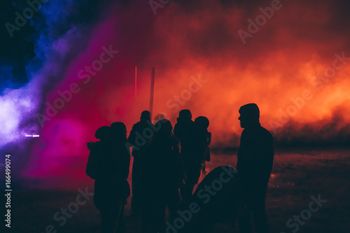 Silhouettes of people standing in front of a colorful smoke photo