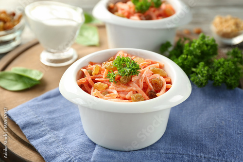 Bowl with delicious carrot raisin salad on wooden board