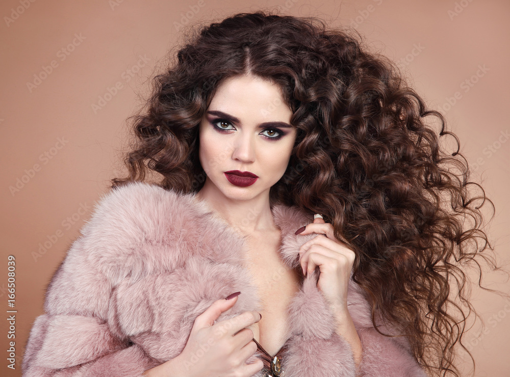 Healthy Beauty hair. Glamour portrait of beautiful brunette woman model with marsala matte lips makeup and long curly hairstyle in luxury fur coat isolated on beige background Healthy Beauty hair. Glamour portrait of beautiful brunette woman model with marsala matte lips makeup and long curly hairstyle in luxury fur coat isolated on beige background
