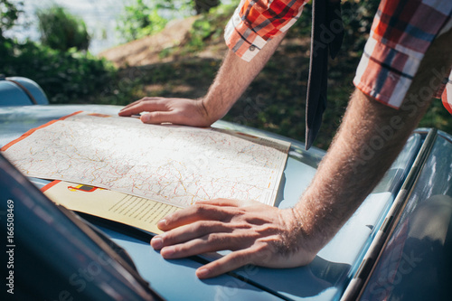 Close Up of Young Man Looking at Road Map on Car Hood photo