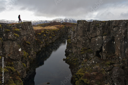 A lone figure stands on the edge of a canyon in the Thingvellir National Park, Iceland