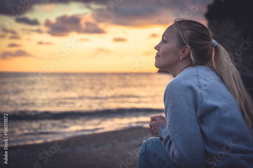 Pensive lonely smiling woman looking with hope into horizon during sunset at beach photo