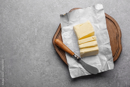 Fotografie Cutting board with piece of unwrapped sliced butter and knife on grey background