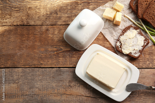 Piece of butter in dish, knife and delicious toast on wooden table