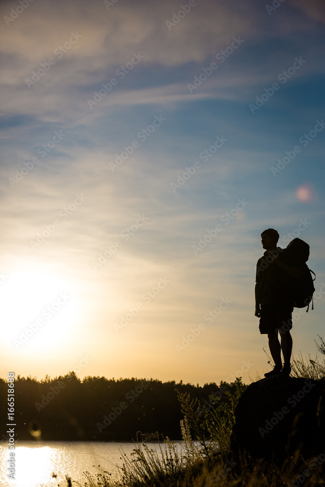 Young tourist with backpack standing on a rock and enjoying sunset