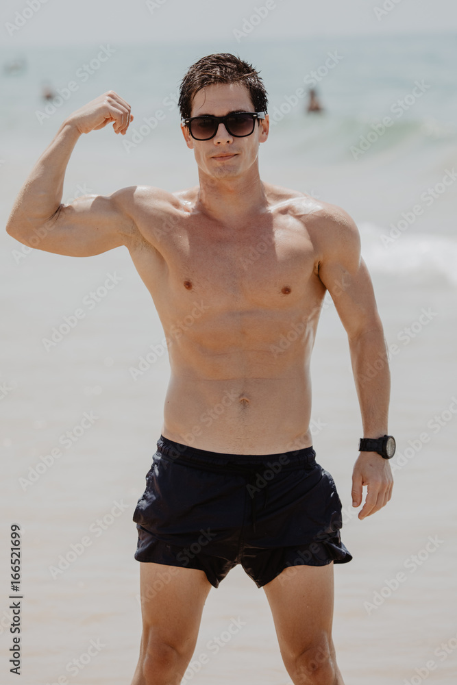 Muscular Hawaiian man walking on the beach as ocean waves crash behind