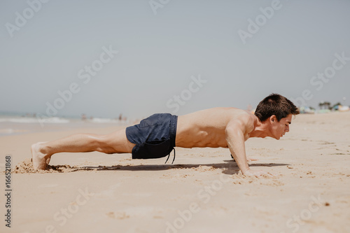 fitness man exercising push ups smiling happy. Male fitness model cross-training on beach.