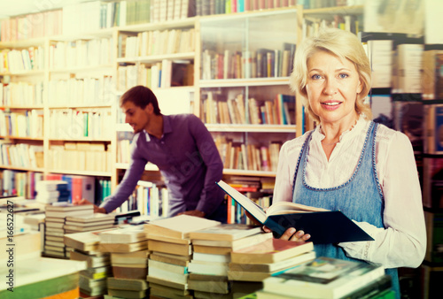 Smiling mature woman reading book in book shop