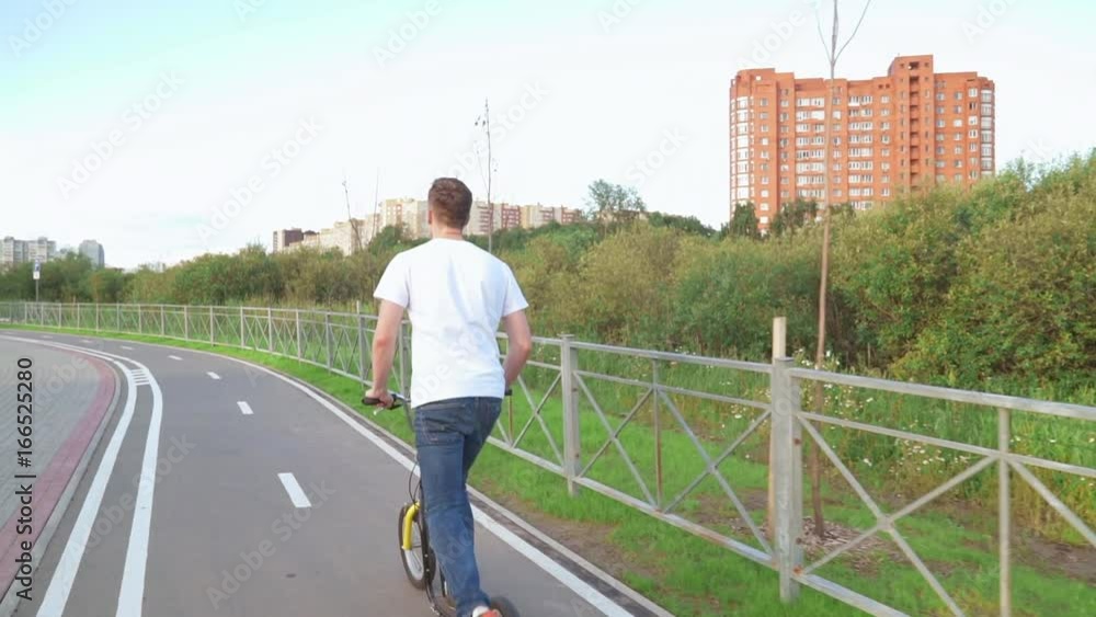 A man is riding a kick scooter in the park A man is riding a kick scooter in the park