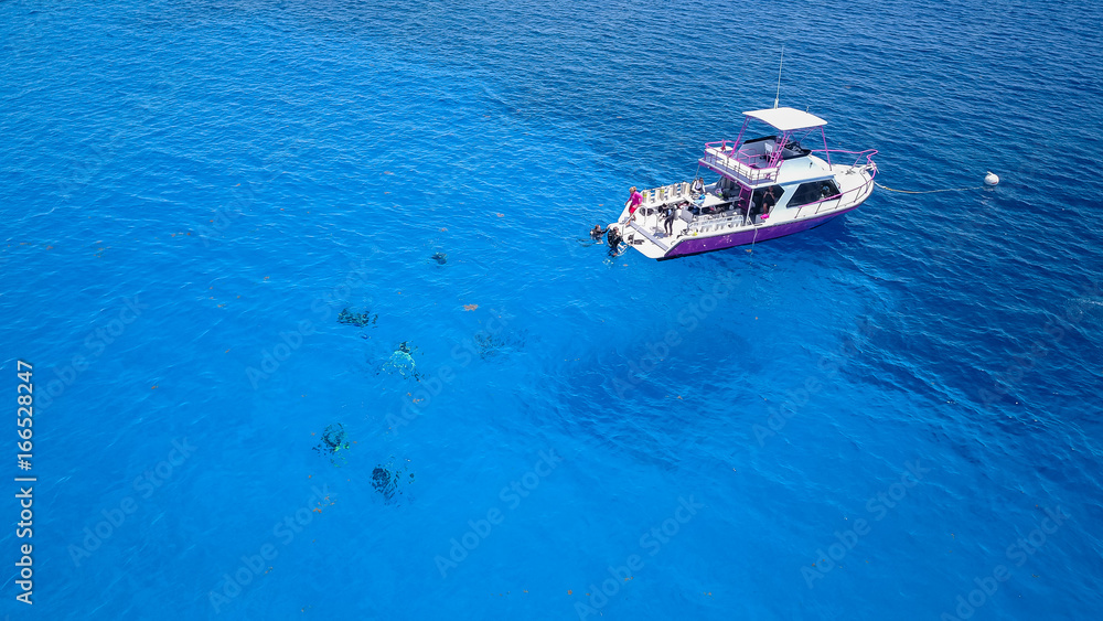 SCUBA divers and a dive boat in clear, blue, tropical waters viewed from the air