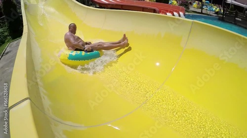 Adult man rides a yellow slide in aquapark,  photo