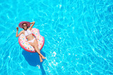 Beautiful young woman with inflatable donut in blue swimming pool
