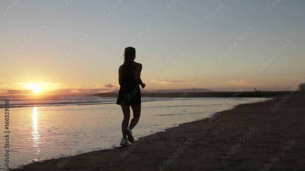 Young woman running on the beach near the ocean at sunset glidecam Young woman running on the beach near the ocean at sunset glidecam