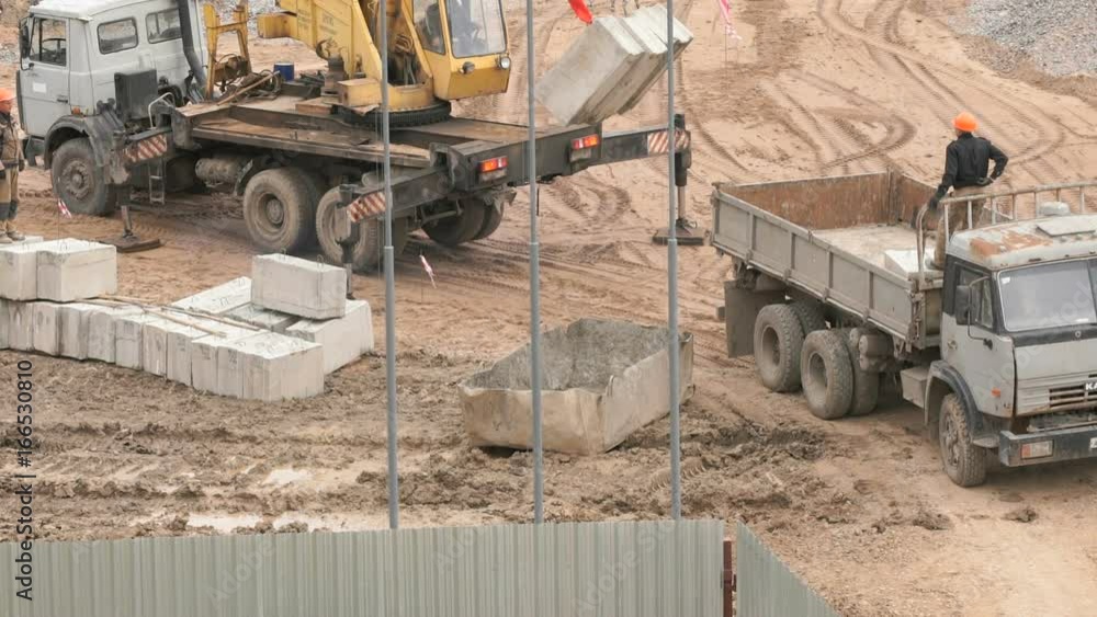 Builder dressed in orange helmet provides uploading of foundation blocks on the dump truck. Construction site Builder dressed in orange helmet provides uploading of foundation blocks on the dump truck. Construction site
