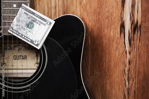 Black guitar close-up with five dollars
