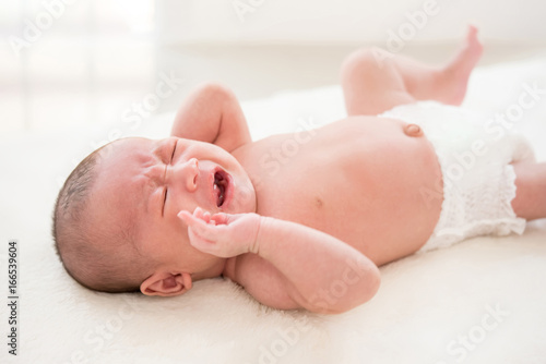 Shirtless newborn baby lying and crying on the bed