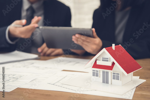 Real estate agent discussing work with blueprints and house model on the table