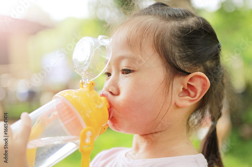 Close Up little girl drinking water from bottle in the park. Portrait outdoor.