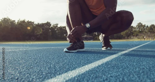 Young male athlete tying up shoes on a running track