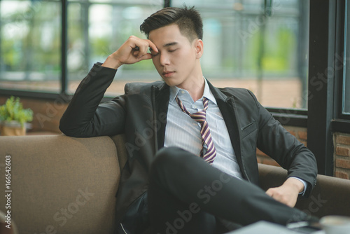 Young attractive Asian business man sleeping, drowsing or taking a nap at her desk, Tired business woman accountant with bills and paper folders in office, tired young business woman with laptop.