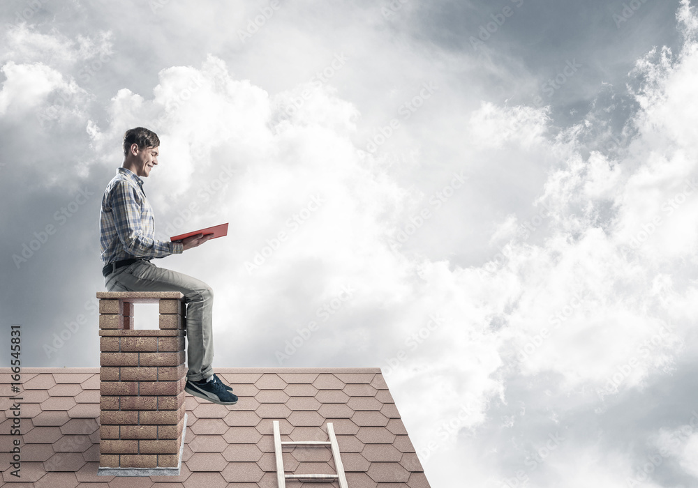 Handsome man on brick roof against cloud scape reading book Handsome man on brick roof against cloud scape reading book