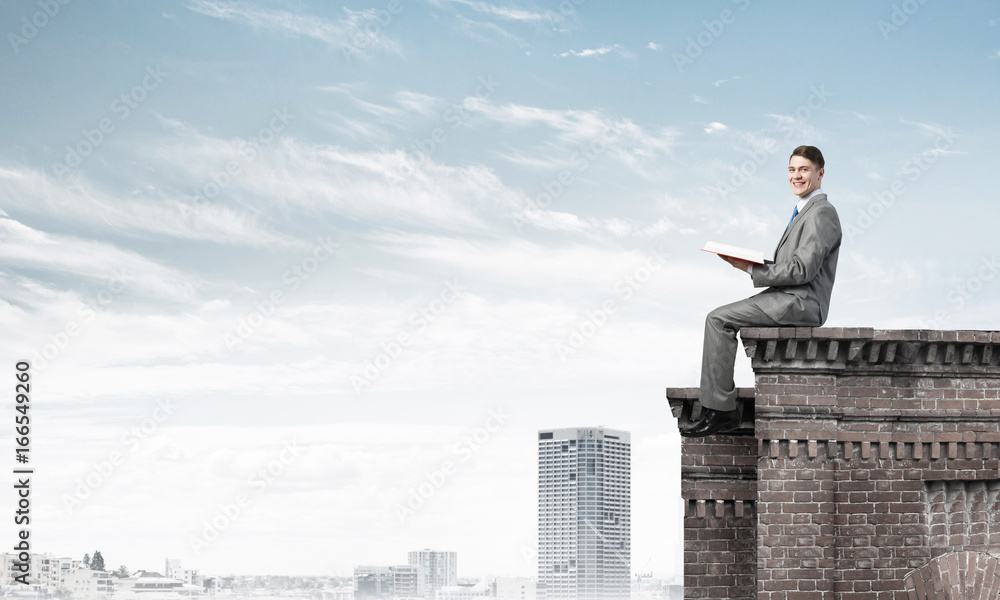 Man on roof edge reading book and cityscape at background Man on roof edge reading book and cityscape at background