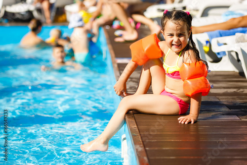 Cute smiling little girl sitting near swimming pool