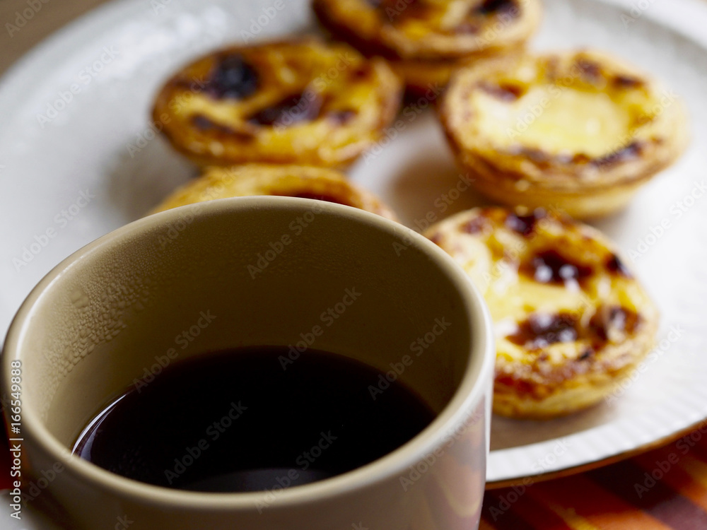 Softfocus custard tarts in a plate and black coffee cup Softfocus custard tarts in a plate and black coffee cup