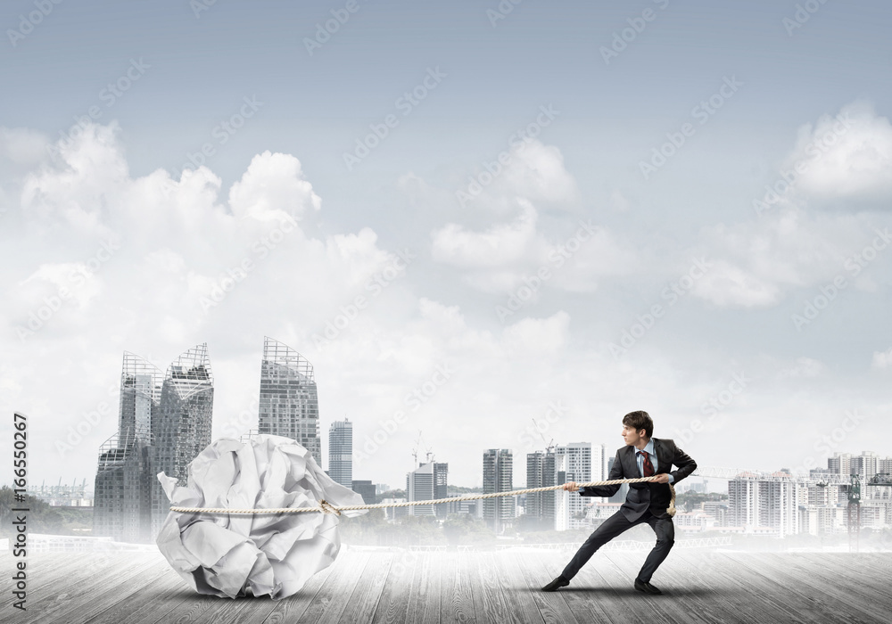 Man pulling with effort big crumpled ball of paper as creativity sign Man pulling with effort big crumpled ball of paper as creativity sign
