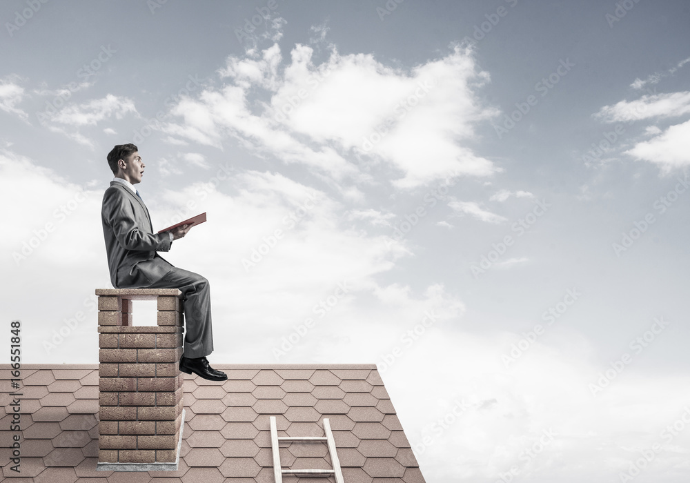 Student guy in suit on brick house roof reading book Student guy in suit on brick house roof reading book