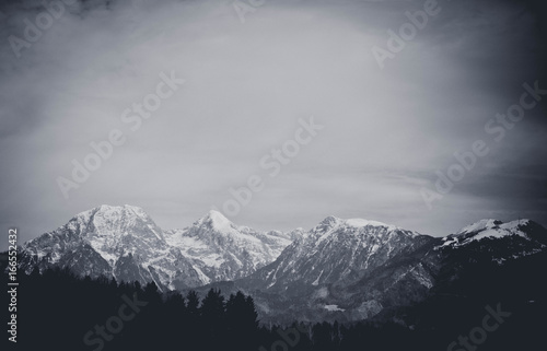 Photo depicting a beautiful moody frosty landscape. European alpine mountains with snow peaks on a blue sky background. Black and white.