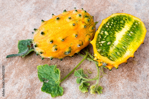 two fresh ripe kiwano with vine and leaves, Cucumis metuliferus, on ceramic background